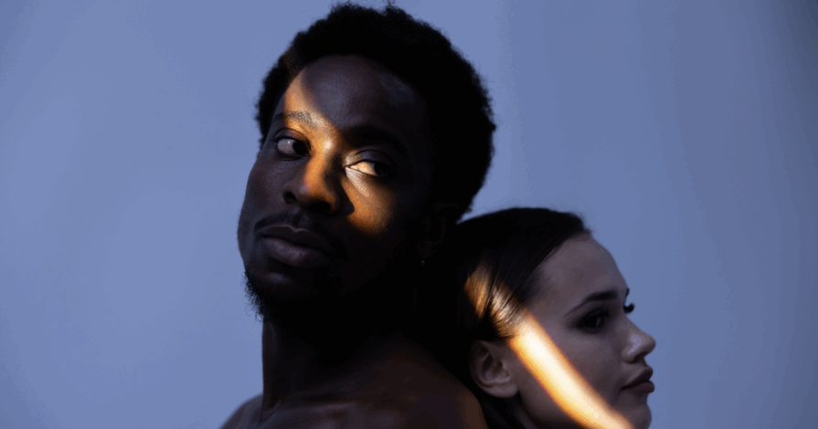 Afro man en brunette vrouw in de schaduw tegen een grauwe achtergrond ter illustratie van de relatieproblemen