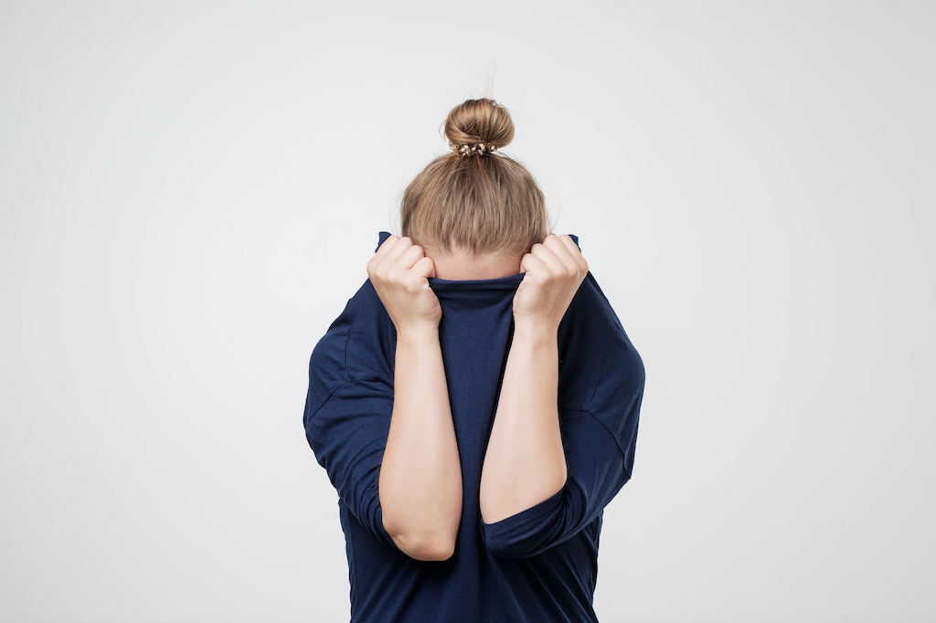 vrouw met knotje trekt de trui over har gezicht uit schaamte