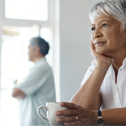 vrouw met kop koffie denkt na over grijze scheiding en AOW na scheiding terwijl partner op afstand staat