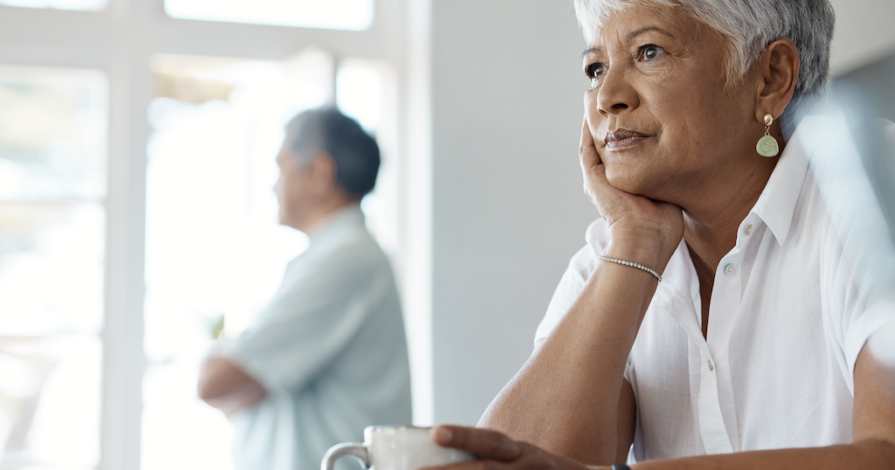 vrouw met kop koffie denkt na over grijze scheiding en AOW na scheiding terwijl partner op afstand staat