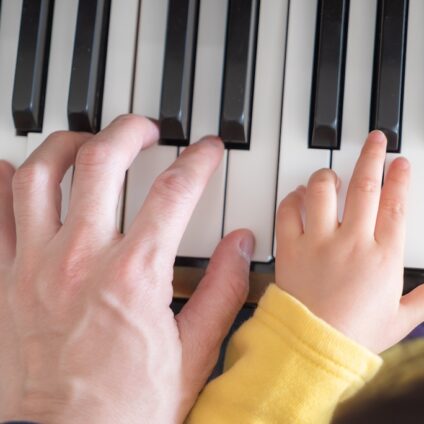 Een volwassen hand en een kinderhand spelen samen op een piano.