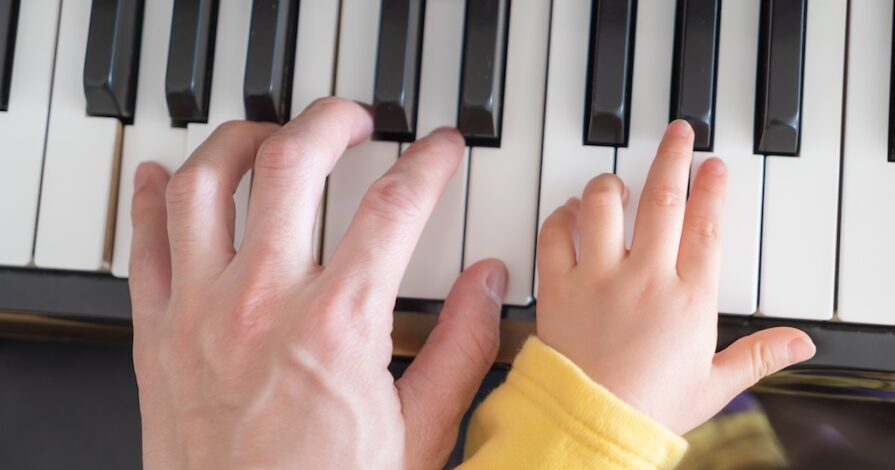 Een volwassen hand en een kinderhand spelen samen op een piano.